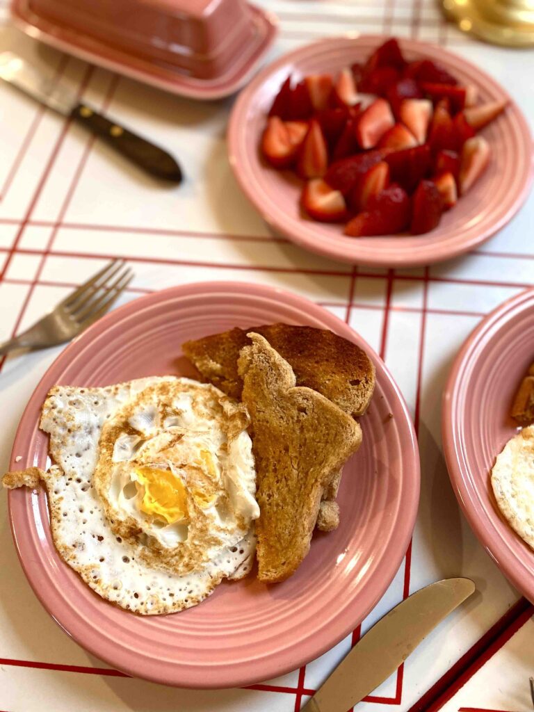 breakfast spread with over easy eggs, toast, and strawberries in the backbround